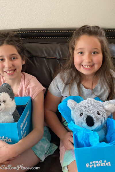 Girls holding 2 Send a Friend plush toys